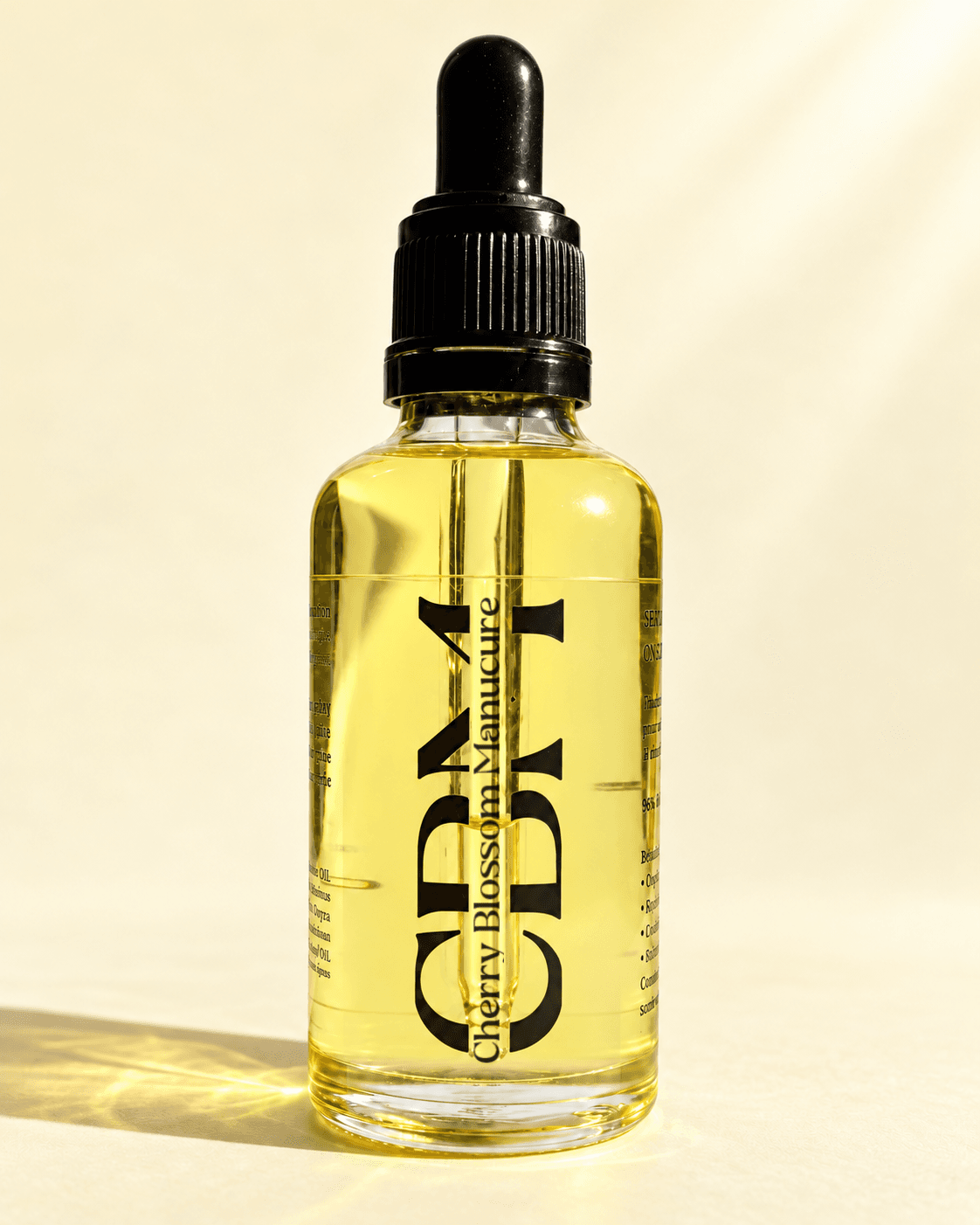 Flacon de Sérum fortifiant CBM 50 ml pour le soin des ongles et cuticules, huile nourrissante dorée avec pipette noire sur fond crème.