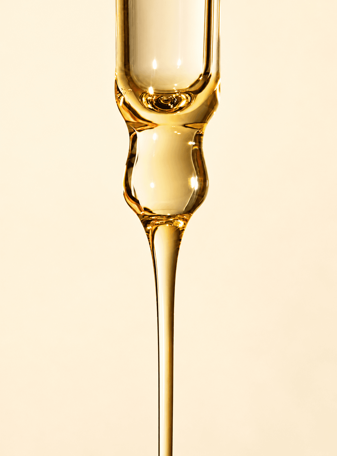 Gros plan d'une pipette en verre laissant couler une huile dorée, texture du Sérum fortifiant pour ongles et cuticules CBM sur fond crème.